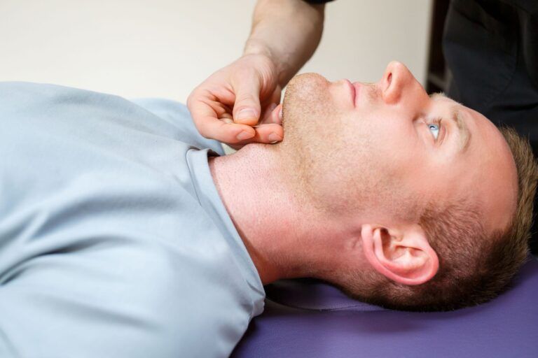 A skilled chiropractor uses manual techniques on a patients jaw while they lie on a treatment table,