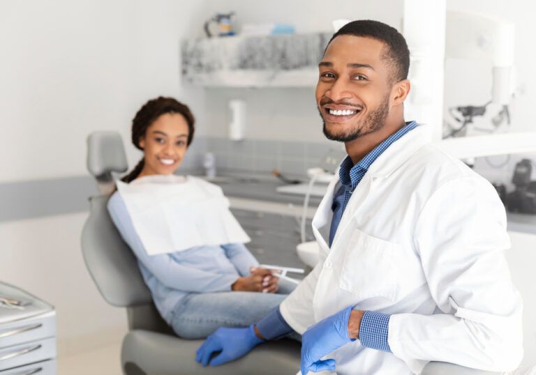 Visiting dentist. Black dentist doctor and female patient in chair smiling at camera, clinic interior
