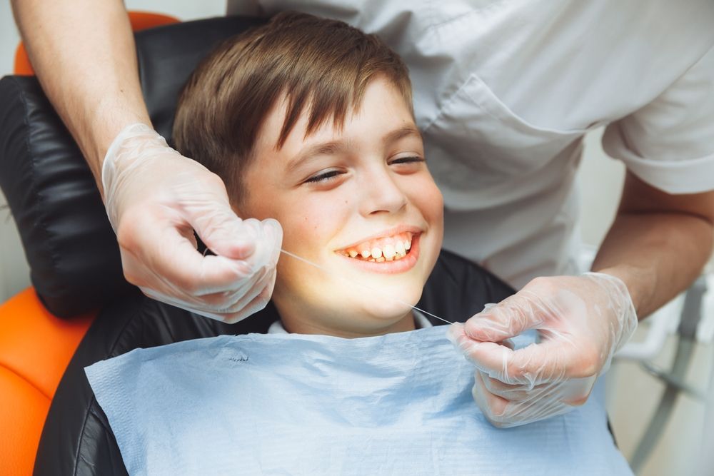 the dentist brushes the boy's teeth with dental floss