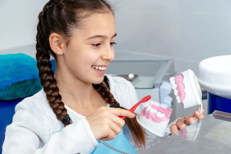 Girl in dentist's office shows how to brushing your teeth