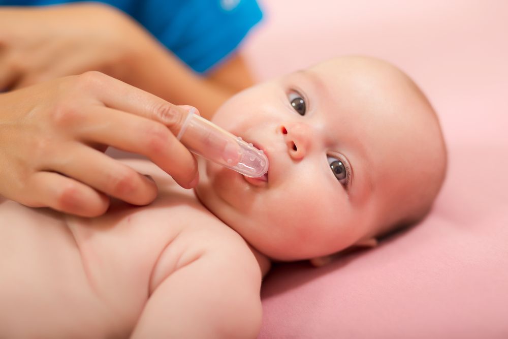 Mother cleaning baby`s mouth with special fingertip brush for children