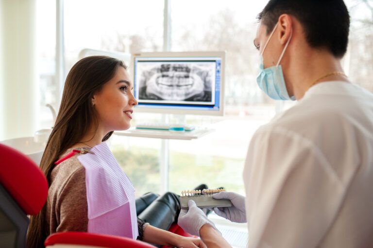 The dentist selects the color of dental implants for a beautiful girl.
