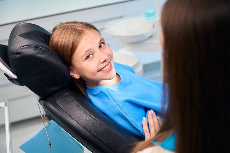 Smiling teenage girl communicates with female hygienist in dental office