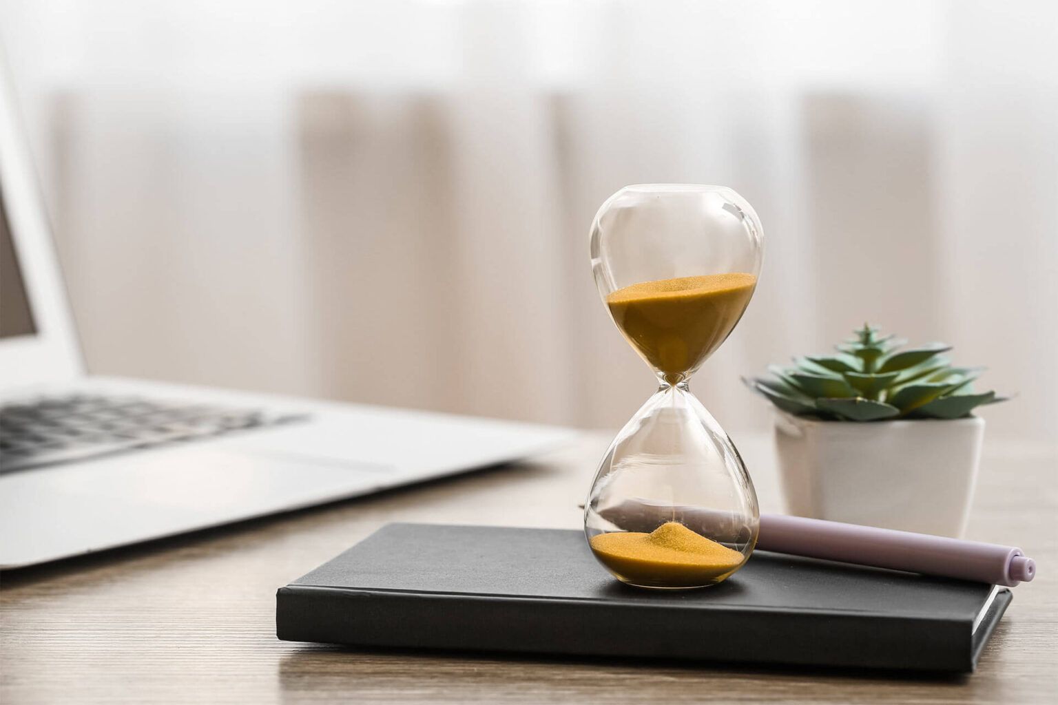 Hourglass with laptop, notebook and succulent on table in office