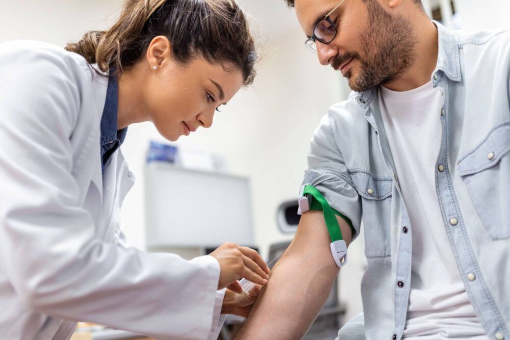 Friendly hospital phlebotomist collecting blood sample from patient in lab