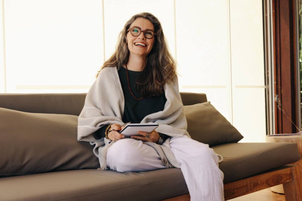 Journaling and mental wellbeing. Mature woman smiling happily while writing and entry in her diary at home.