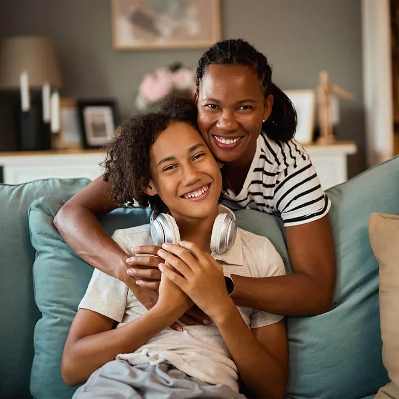 Portrait of embraced teenage boy and his mother at home