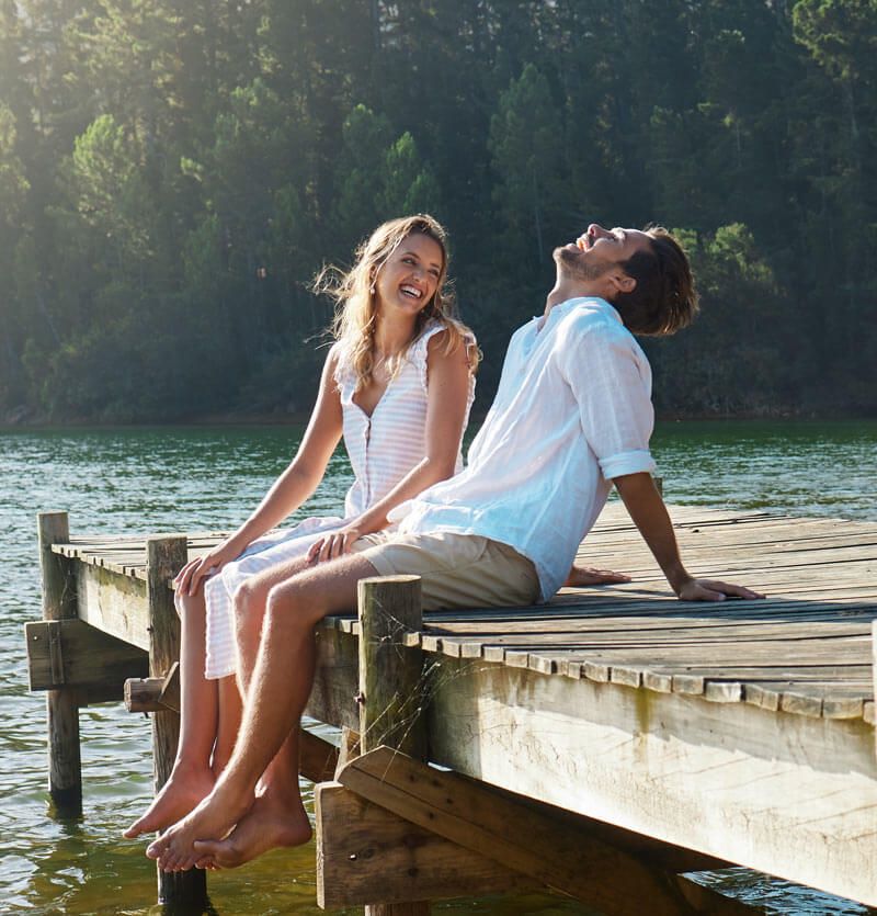 Young couple, lake and jetty with laughing, happiness and bonding with love in nature for holiday