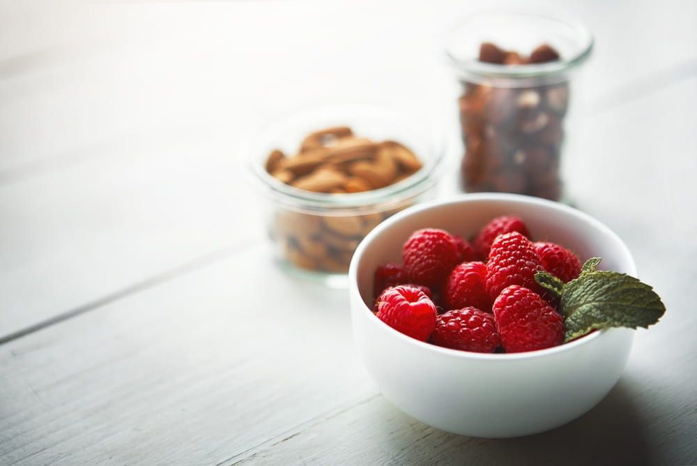 Table, wellness and nuts with berries in bowls for natural nutrition, plant based foods and protein. Health, raspberries and almonds in house for healthy snacks, antioxidants and vitamins