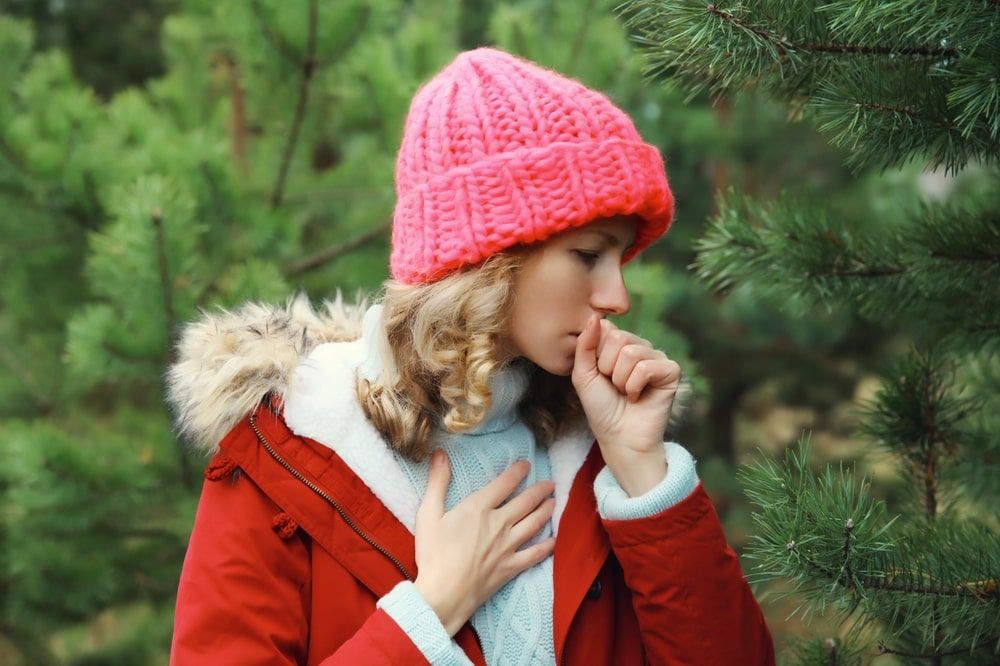 Cold and health, sick young woman coughing outdoors in winter park near tree