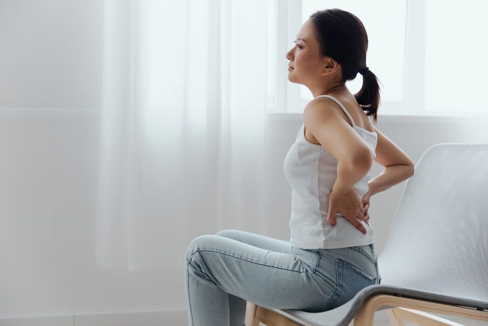 Asian woman feel hurt joint back pain laptop in incorrect posture sit on chair.