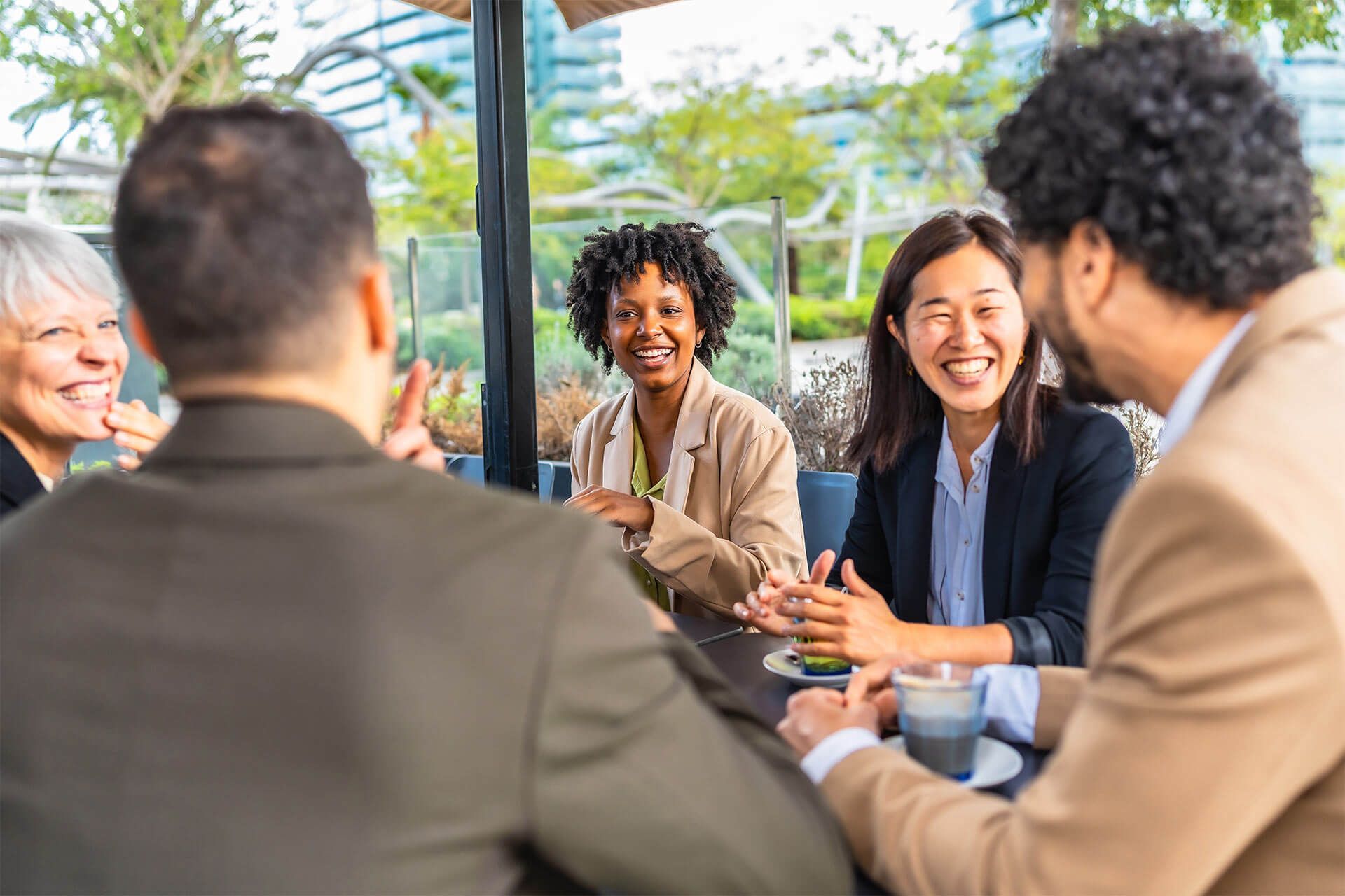 Smiling businesswomen talking with multi-ethnic colleagues sitting drinking coffee in a cafeteria
