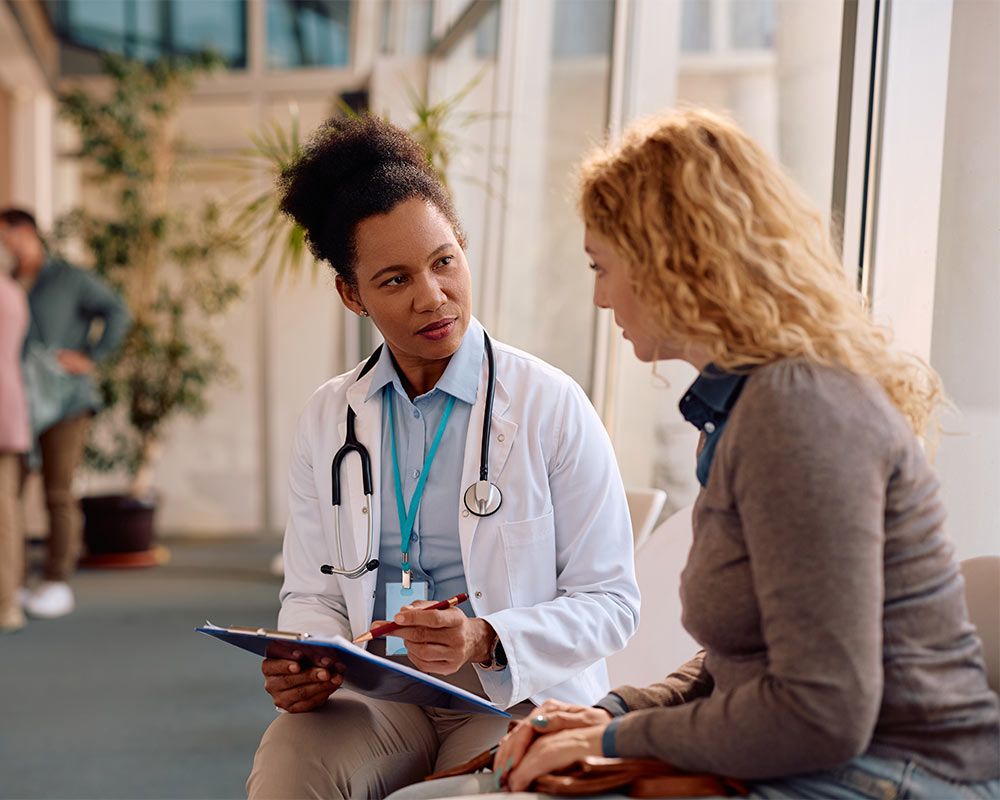 African American doctor and her female patient analyzing test results after medical examination at polyclinic.