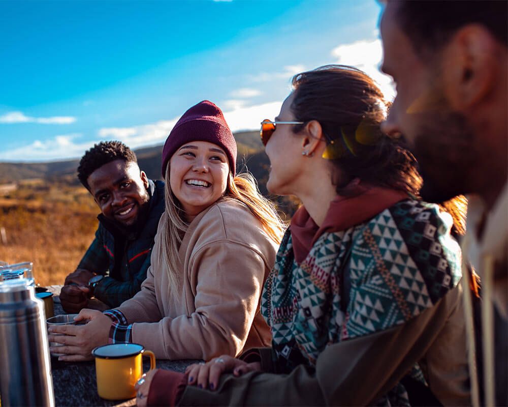 Group of friends sitting on the top of the hill at bench resting after hiking and drinking tea.