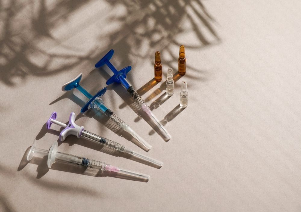 flat lay of various syringes, ampoules, medical gloves, disposable cap, light background, natural sunlight.