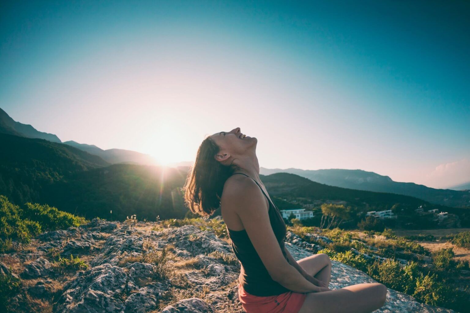 A girl is sitting on top of a mountain and laughing. A smiling woman admires the beauty of nature