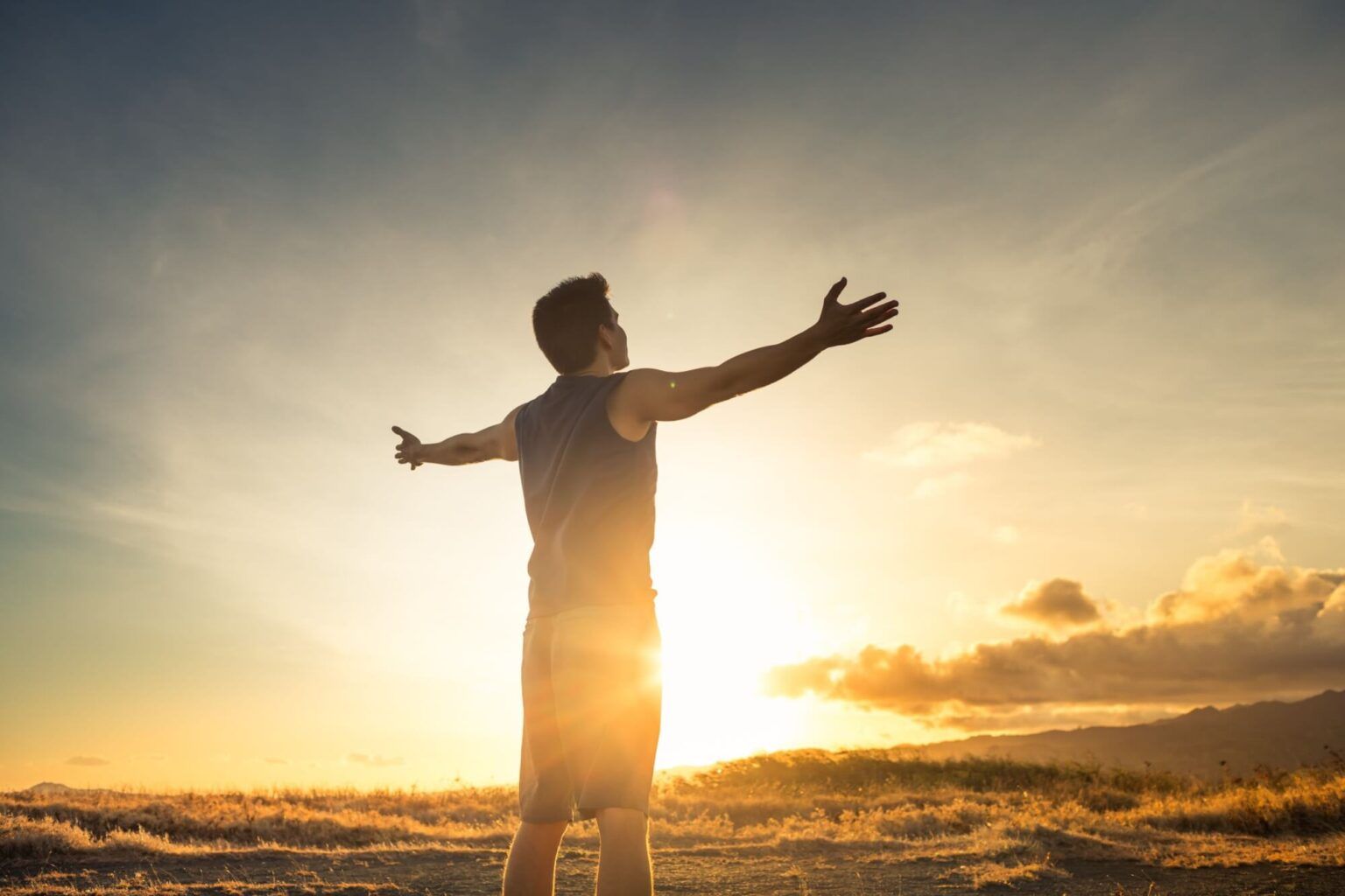 Happiness bliss freedom concept. Young man happy feeling joyful with arms up facing the mountain sunrise.