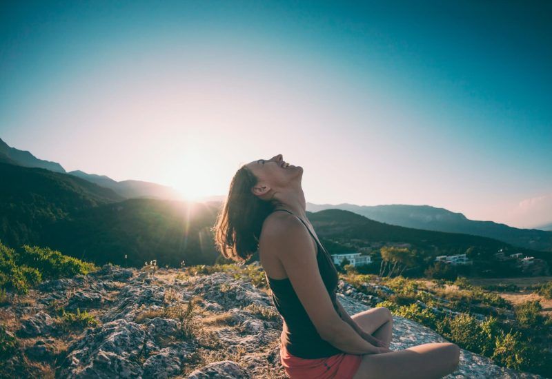 A girl is sitting on top of a mountain and laughing. A smiling woman admires the beauty of nature