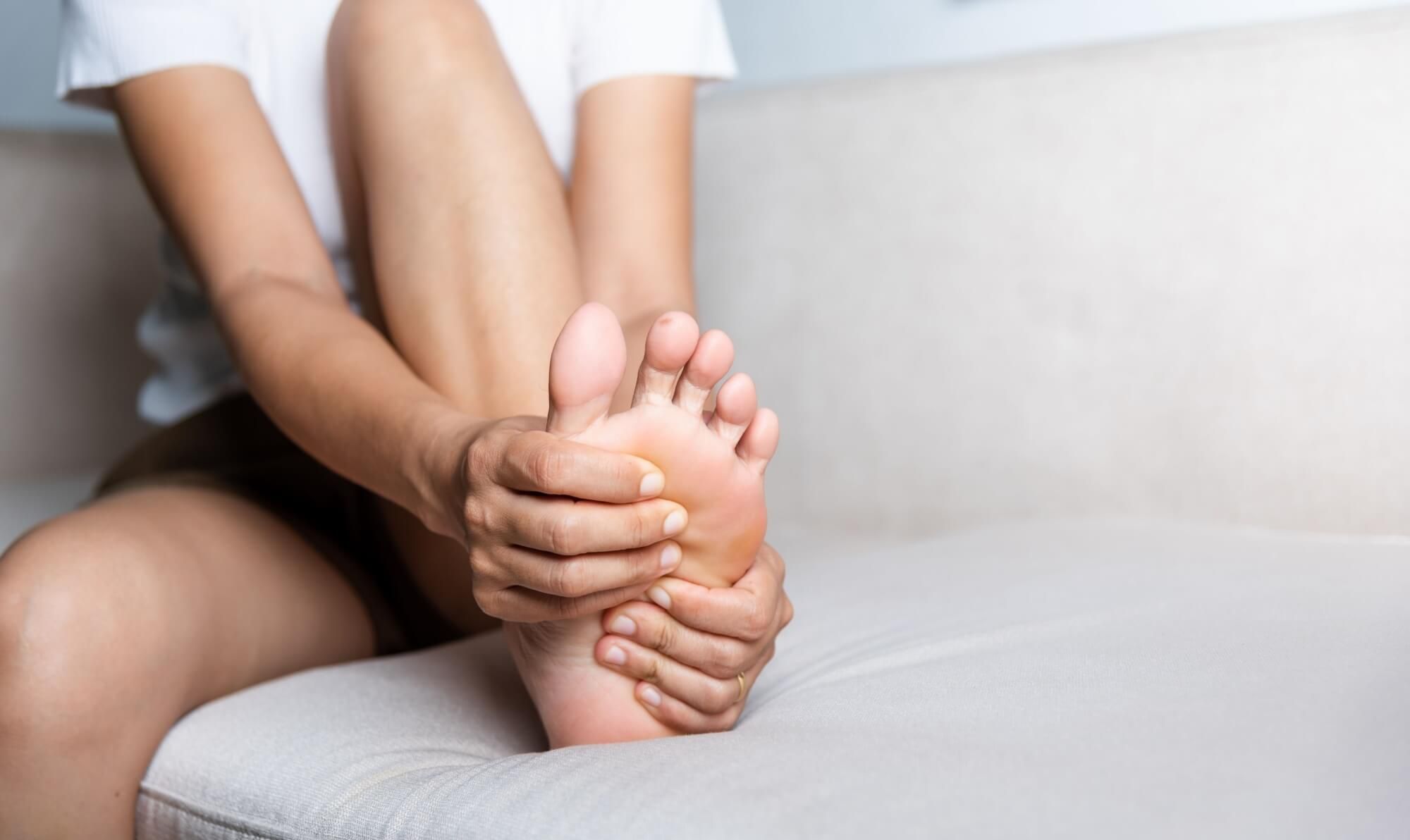 Foot pain, Asian woman sitting on sofa feeling pain in her foot at home
