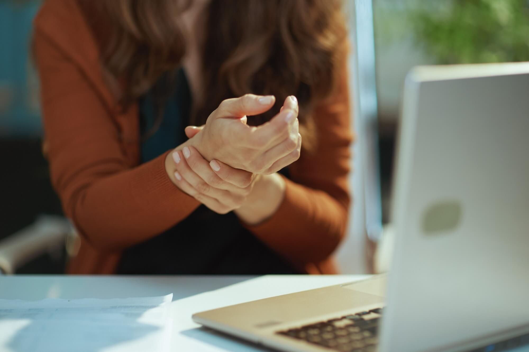 Closeup on small business owner woman with laptop experience carpal syndrome in the green office.