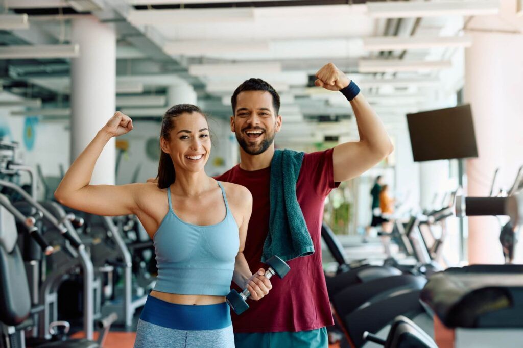 Happy athletic couple flexing their muscles after working out in a gym and looking at camera.