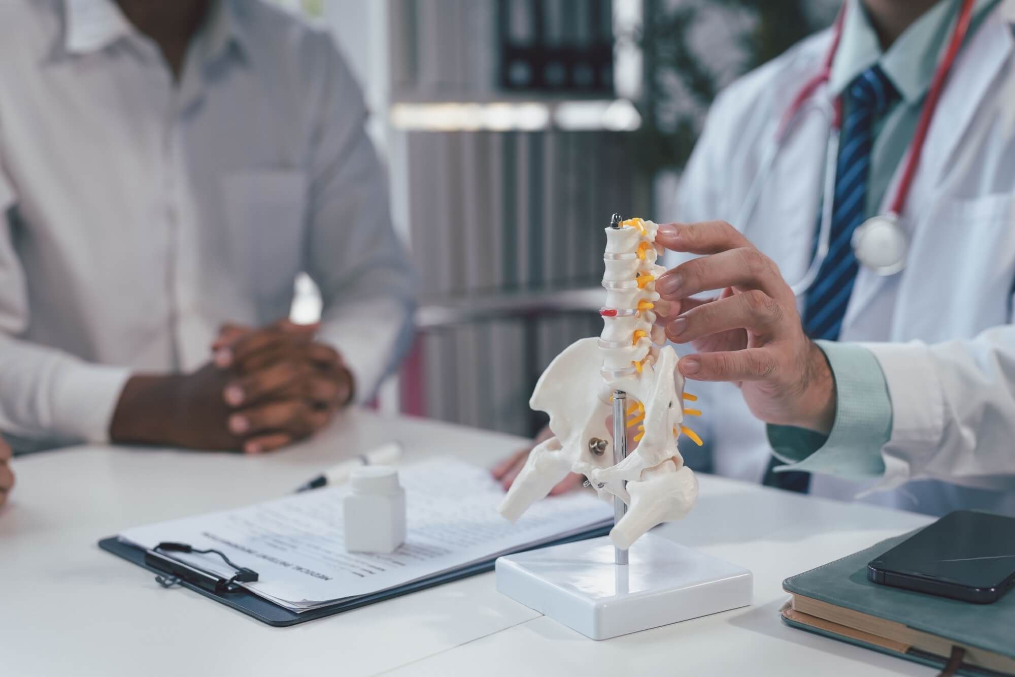 Doctor explaining spine anatomy to a patient in a hospital office. Close-up shows professional care in diagnosing spine issues