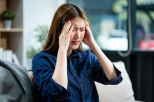 A young Asian woman sits on a sofa in her living room, feeling sick with a headache