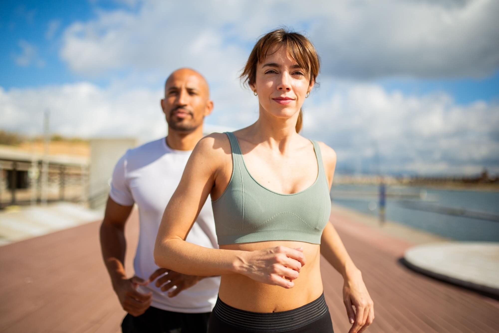 determined woman and her running partner jogging by the waterfront, embracing an active lifestyle under a vibrant sky.