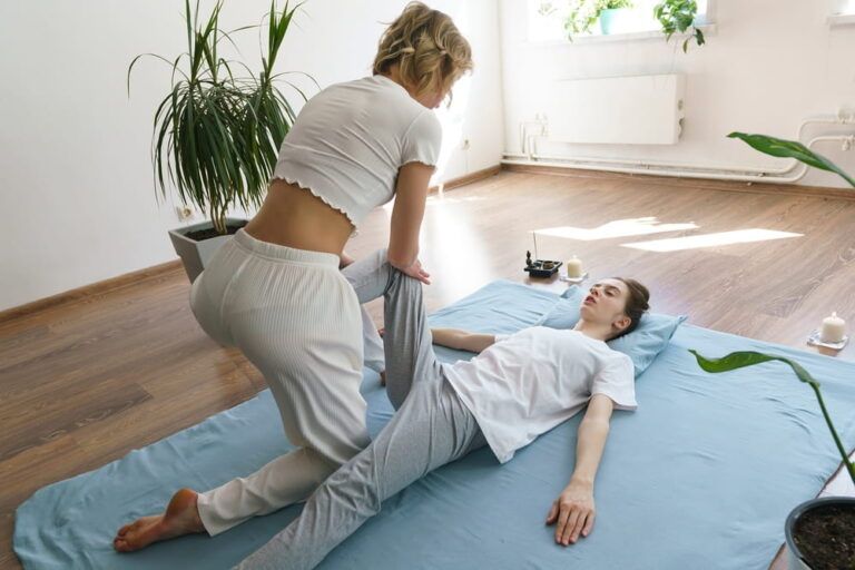 a young masseuse does a Thai massage on the floor massaging her hip and pelvic joints