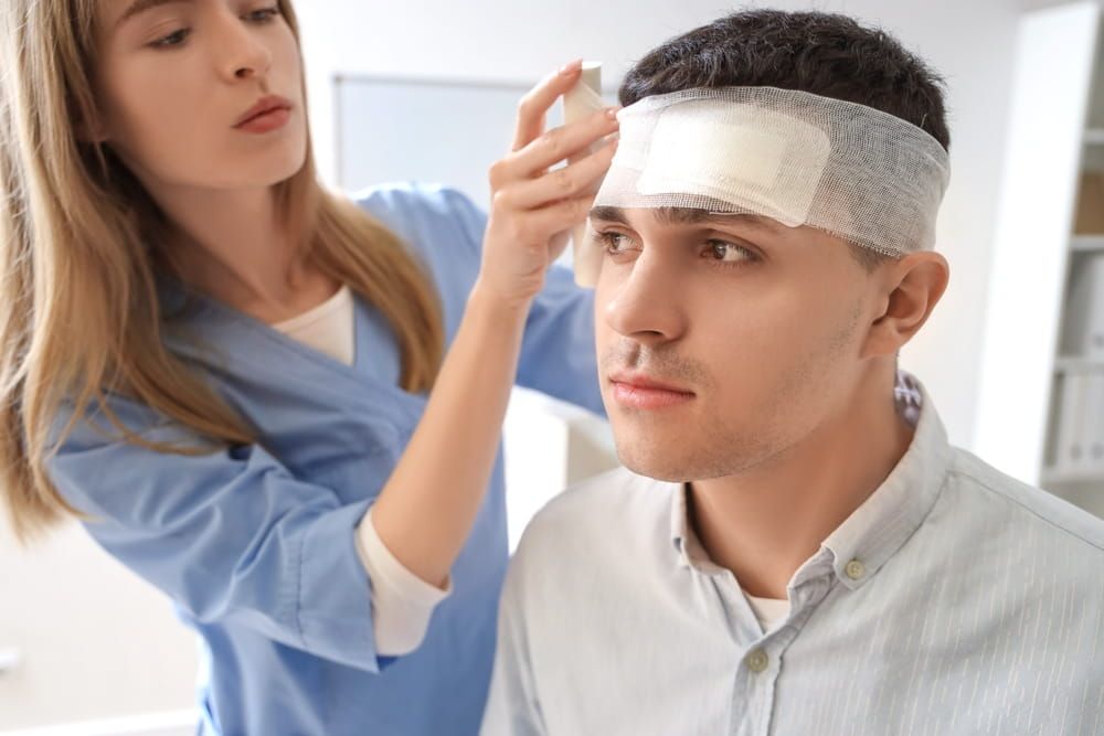Female doctor bandaging man's head with brain concussion in clinic, closeup