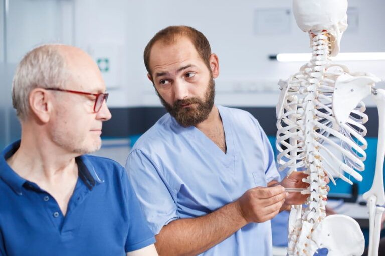 Chiropractor shows spinal cord bones to senior man for orthopedic diagnosis and physical therapy